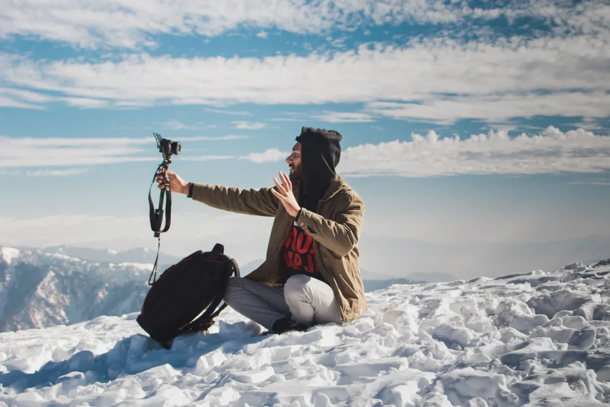 Un viajero se graba con una cámara en tripié, sentado en la cima de una montaña nevada